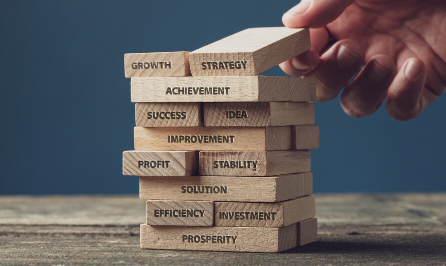 Wide view image of businessman stacking wooden pegs with words of business development and success written on them. Over blue background.